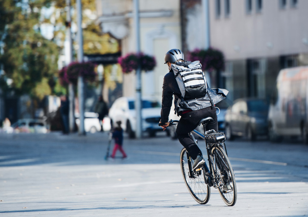 an electric biking being ridden away through the city on a sunny day